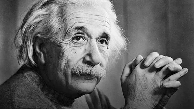 : "Ünlü fizikçi Albert Einstein'ın ellerini çenesinin altında birleştirmiş, hafifçe yukarıya doğru bakan düşünceli bir ifadeye sahip siyah beyaz portresi."