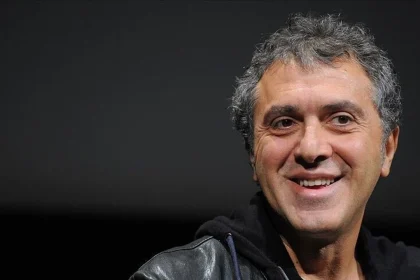 Reha Erdem gülümserken yakın plan portre, koyu arka plan önünde yönetmen görüntüsü